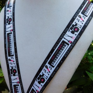 May include: Black and white ribbon with a musical theme. The ribbon features illustrations of musical instruments like keyboards, drums, and microphones, along with musical notes. The words "ROCK STAR" are printed repeatedly along the edges of the ribbon.