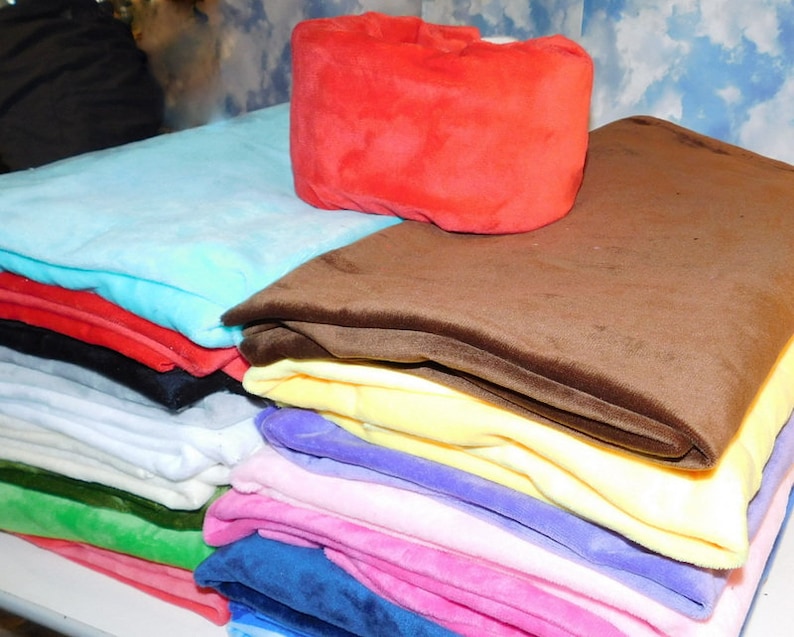 May include: A stack of fabric swatches in various colors, including red, brown, yellow, blue, pink, and green. The fabric is soft and plush, with a velvety texture.