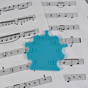 May include: A blue plastic tool with a star shape and numbers from 9 to 12.5 printed on it. The tool is used for measuring the size of guitar strings.