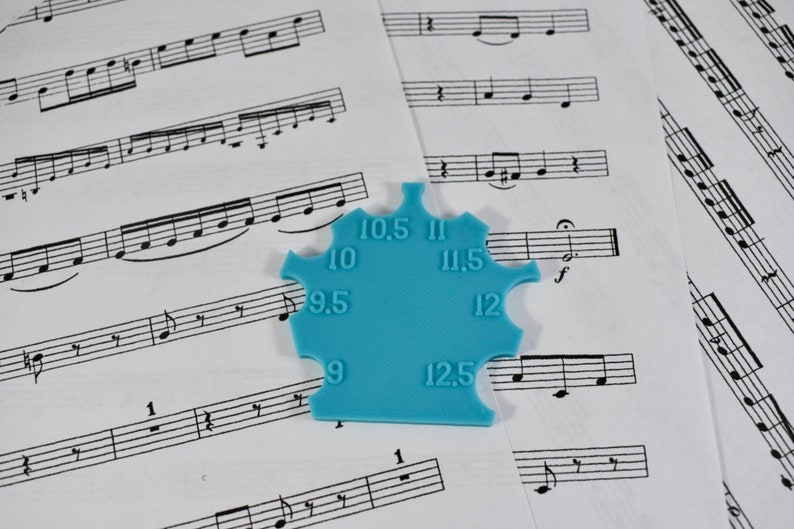 May include: A blue plastic tool with a star shape and numbers from 9 to 12.5 printed on it. The tool is used for measuring the size of guitar strings.