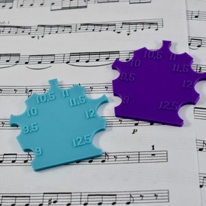 May include: Two plastic ring sizers, one blue and one purple, with measurements from 9 to 12.5. The sizers are on a sheet of music.