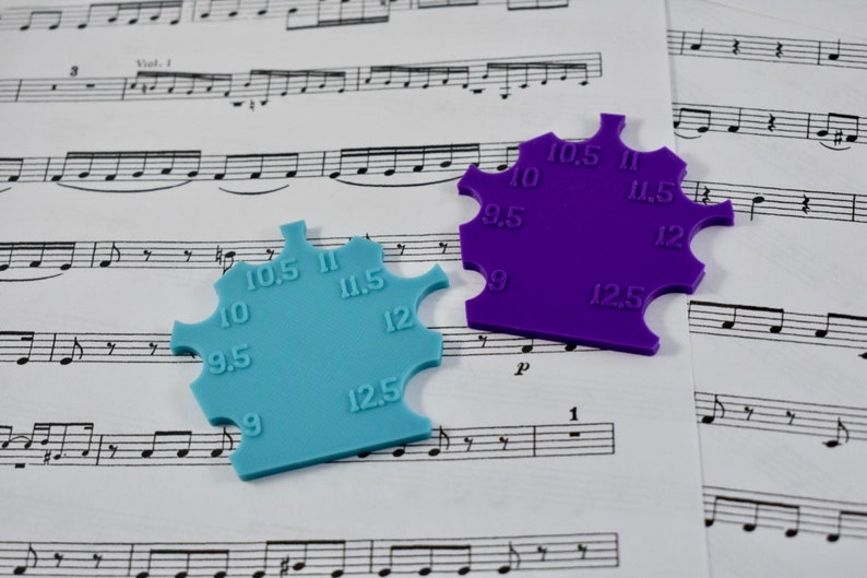 May include: Two plastic ring sizers, one blue and one purple, with measurements from 9 to 12.5. The sizers are on a sheet of music.