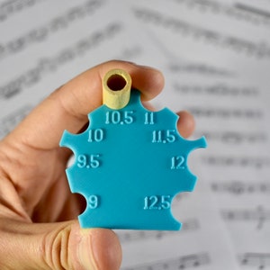 May include: A blue plastic tool with a round hole at the top and numbers from 9 to 12.5 around the edge. The tool is used to measure the size of a hole.