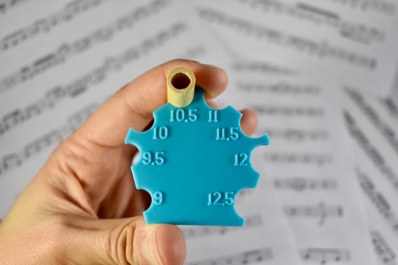 May include: A blue plastic tool with a round hole at the top and numbers from 9 to 12.5 around the edge. The tool is used to measure the size of a hole.