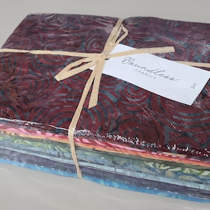 May include: A stack of 10 fabric squares wrapped in plastic with a brown ribbon and a white tag that says "Boundless Fabrics". The fabric squares are various shades of blue, green, orange, and pink with a batik pattern.