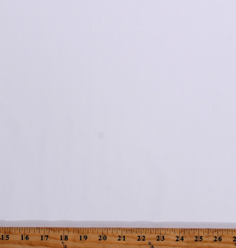 Puede incluir: Una muestra de tela blanca con una regla de madera que mide 66 cm.