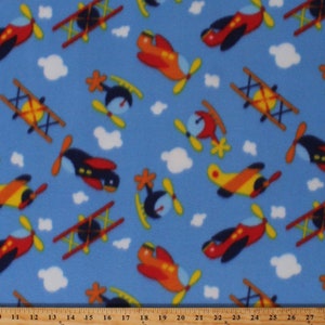 May include: A blue fabric with a repeating pattern of airplanes in various colors and styles. The airplanes include red, yellow, blue, and orange planes. There are also white clouds in the background.