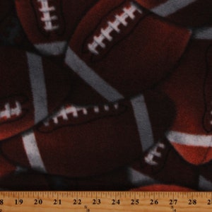 May include: Close-up of brown and white fleece fabric with a repeating pattern of American footballs.