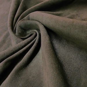 May include: Close-up of dark olive green fabric with a soft texture. The material is gathered and swirled, creating folds and shadows. The fabric appears to be a knit or jersey material, suitable for clothing or home decor.