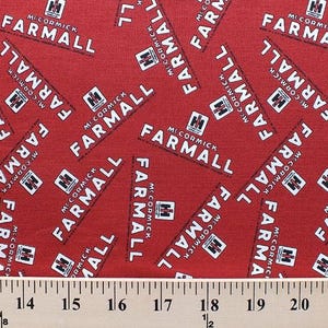 May include: Red fabric with a repeating pattern of white "McCormick Farmall" logos. The fabric is measured with a ruler in inches.
