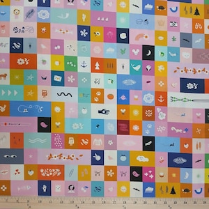 May include: A colorful fabric with a patchwork design featuring various illustrations. The squares contain images of animals, flowers, and other whimsical elements in shades of pink, blue, yellow, and orange. The fabric has a ruler at the bottom.