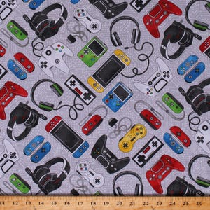 May include: A gray fabric with a repeating pattern of video game controllers, headsets, and game consoles. The pattern includes various colors such as red, blue, green, yellow, and black.