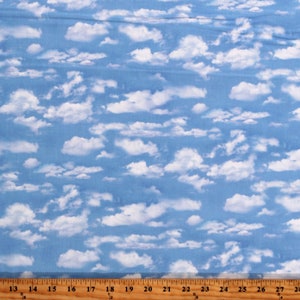 May include: Blue fabric with a white cloud pattern. The fabric has a light blue background with various sizes of fluffy white clouds. A wooden ruler is at the bottom of the image, with inch measurements.