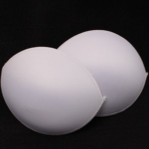 May include: Two white foam bra inserts, designed to add volume and shape to a bra. The inserts are smooth and seamless, with a rounded shape.