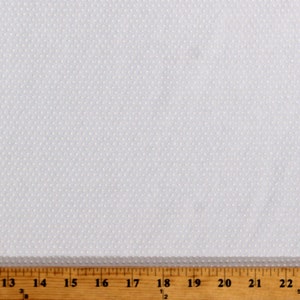 May include: White fabric with a small white dot pattern. The fabric is measured with a ruler in inches.