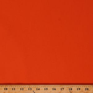 May include: A solid orange fabric with a smooth texture. The fabric is a vibrant shade of orange, and a ruler is at the bottom of the image, with measurements in inches.