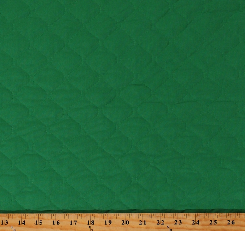 May include: A close-up of a green quilted fabric with a diamond pattern. The fabric is measured with a ruler in inches.