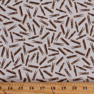 May include: A white fabric with a repeating pattern of brown wooden clothespins. The fabric is measured with a ruler in inches.