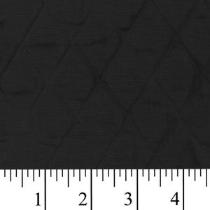 May include: Close-up of black quilted fabric with a diamond pattern. The fabric is measured with an inch ruler, showing the scale of the quilting. The texture appears soft and the color is a solid black.