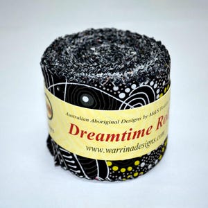 May include: A roll of fabric with a black and white Aboriginal design. The fabric is wrapped with a yellow label that reads "Dreamtime Rolls" and "Australian Aboriginal Designs". The fabric is likely used for quilting or crafting.