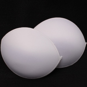 May include: Two white foam bra inserts. The inserts are round and have a smooth, seamless surface. They are designed to add volume and shape to a bra.