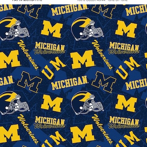 May include: A blue and yellow fabric with a repeating pattern of the University of Michigan logo, including the word "Michigan", "Wolverines", and the letter "M".