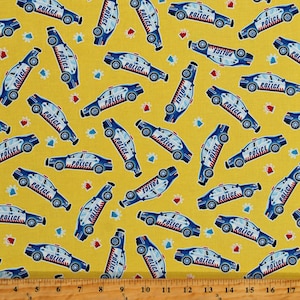 May include: A yellow fabric with a repeating pattern of blue police cars. The cars have white accents and the word "POLICE" printed on the side. The fabric is covered in small blue and red stars.