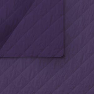 May include: A close-up of a quilted fabric in a deep purple hue. The fabric has a diagonal stitched pattern, creating a textured surface. The corner of the fabric is folded over, revealing the underside and adding depth to the image. The overall effect is a soft, inviting texture.