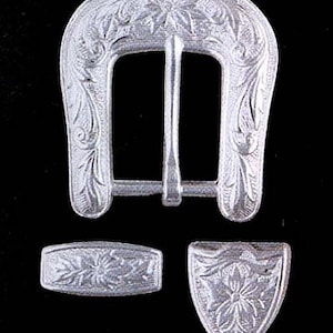 May include: Silver-toned metal belt buckle set with floral and leaf engraving. The set includes a rectangular buckle, a matching belt loop, and a decorative shield-shaped piece. The text "Z1893" is in the upper left corner.