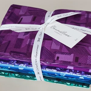 May include: A stack of 12 purple, blue, and green fabric squares tied with a white ribbon. The ribbon has the text "Cut out for happiness" printed on it. A white tag with the text "Boundless Fabrics" is attached to the ribbon.