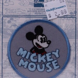 May include: A blue and gray embroidered iron-on patch featuring Mickey Mouse with the text "Mickey Mouse". The patch is on a white background with a price tag that reads "$2.99".
