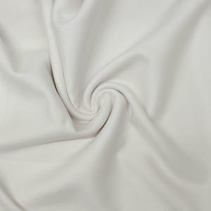 May include: A close-up shot of a white fabric with a soft, flowing texture. The fabric is arranged in gentle folds and a central swirl, creating a sense of movement and depth. The color is a clean, neutral white.