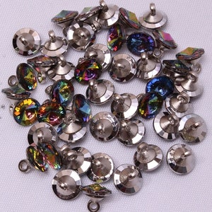 May include: A collection of iridescent crystal buttons with silver-colored metal bases. The buttons have a faceted design that reflects a spectrum of colors, including blues, greens, and yellows. Each button has a loop for sewing.