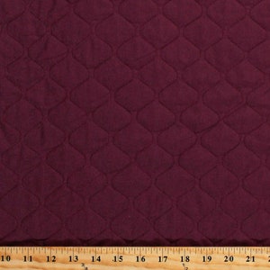 May include: Burgundy quilted fabric with a diamond pattern. The fabric is measured with a ruler in inches.