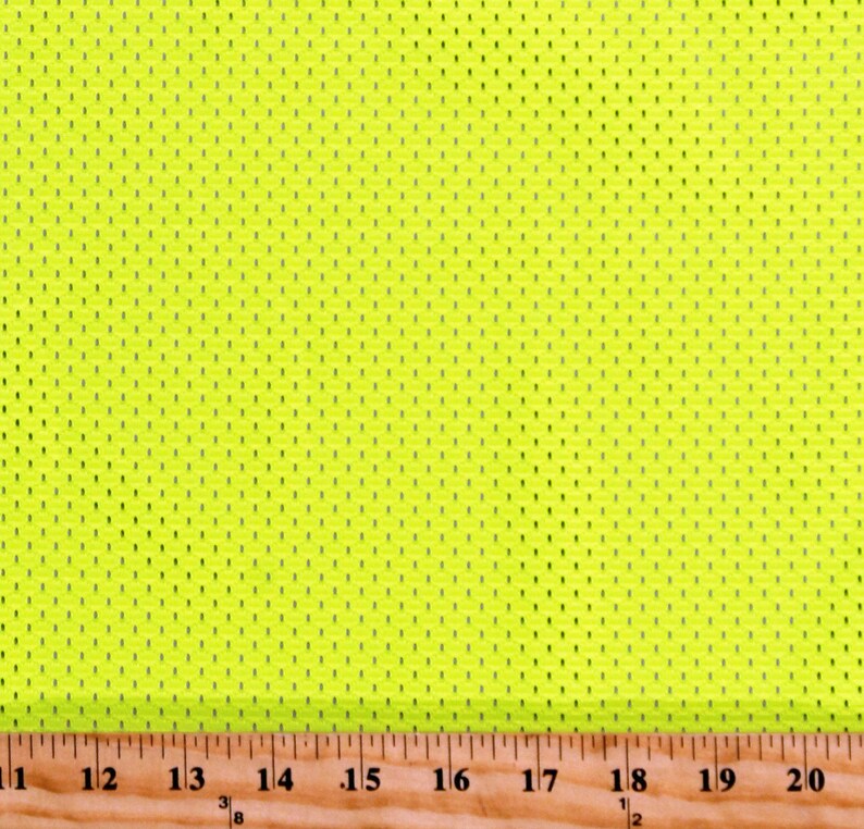 May include: Vibrant neon yellow mesh fabric featuring a pattern of tiny, regularly spaced perforations. The fabric is displayed against a wooden ruler marked in inches, with numbers from 11 to 20.