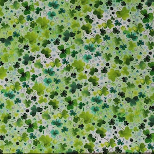 May include: A white fabric with a green watercolor pattern of shamrocks and small white flowers. The fabric is printed with a repeating pattern of shamrocks in various shades of green.