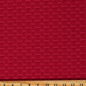 May include: Red textured fabric with a waffle-like pattern. The fabric is shown against a wooden ruler with inch markings.