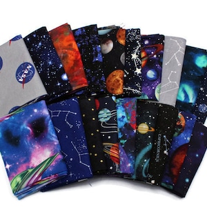 May include: A collection of 15 fabric squares featuring a space theme. The squares are printed with various designs including planets, stars, constellations, and NASA logos. The fabric is a dark blue background with white, silver, and orange accents.