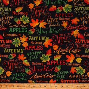 May include: A black fabric with a repeating pattern of fall-themed words and images. The words include "Autumn", "Apples", "Apple Cider", "Nutmeg", "Cinnamon", "Welcome Fall", "Hot Apple Cider", "Thankful", and "Give Thanks". The images include red, orange, and yellow leaves.