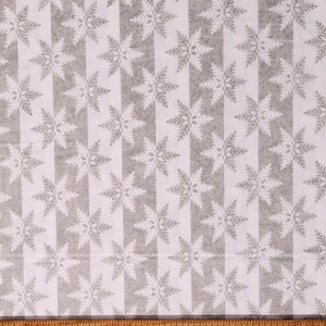 May include: White fabric with a repeating pattern of silver snowflakes on a white background with silver stripes. The fabric is measured with a ruler in inches.