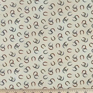 May include: A cream-colored fabric featuring a repeating pattern of small, scattered horseshoes in shades of metallic silver, copper, and dark blue. A wooden ruler is positioned at the bottom, showing measurements in inches.
