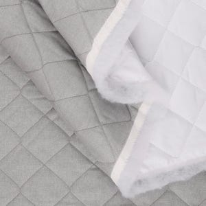 May include: A close-up of a gray quilted fabric with a diamond pattern. The fabric is folded over, revealing a white quilted interior with a fluffy, white edge. The stitching is visible.