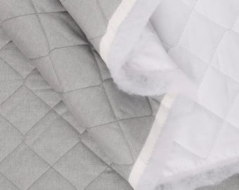 May include: A close-up of a gray quilted fabric with a diamond pattern. The fabric is folded over, revealing a white quilted interior with a fluffy, white edge. The stitching is visible.