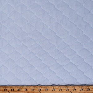 May include: A close-up of a light blue quilted fabric with a diamond pattern. The fabric is measured with a ruler in inches.