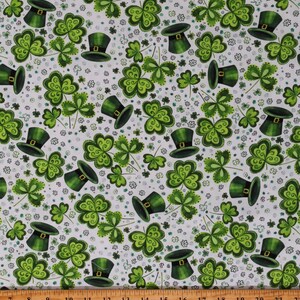 May include: White fabric with a repeating pattern of green shamrocks and green leprechaun hats. The shamrocks have a swirl design and the hats have a gold buckle.