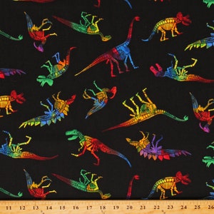 May include: Black fabric featuring a repeating pattern of dinosaur skeletons in vibrant rainbow colors. The dinosaurs are depicted in various poses, with visible ribs and bones. The design includes a ruler along the bottom edge.