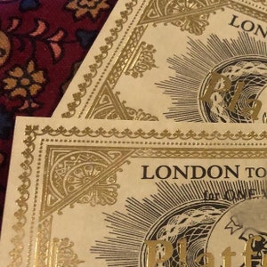 May include: Two rectangular paper tickets featuring gold foil detailing. The text reads LONDON TO and Platform. The design includes intricate gold borders with geometric patterns and sunburst motifs printed on a cream-colored background.
