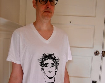 May include: A white v-neck t-shirt with a black and white illustration of a person's face on the front.