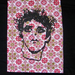 May include: A canvas print featuring a black and white sketch of a face. The background is a repeating pattern of red, green, and white floral designs. The artwork is set against a black background.