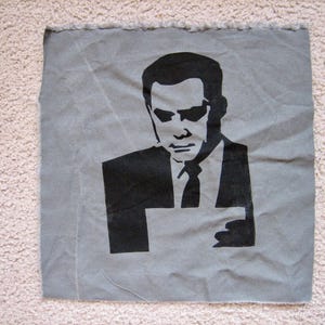 May include: A black and white image of a man wearing a suit and sunglasses. The image is printed on a gray fabric.